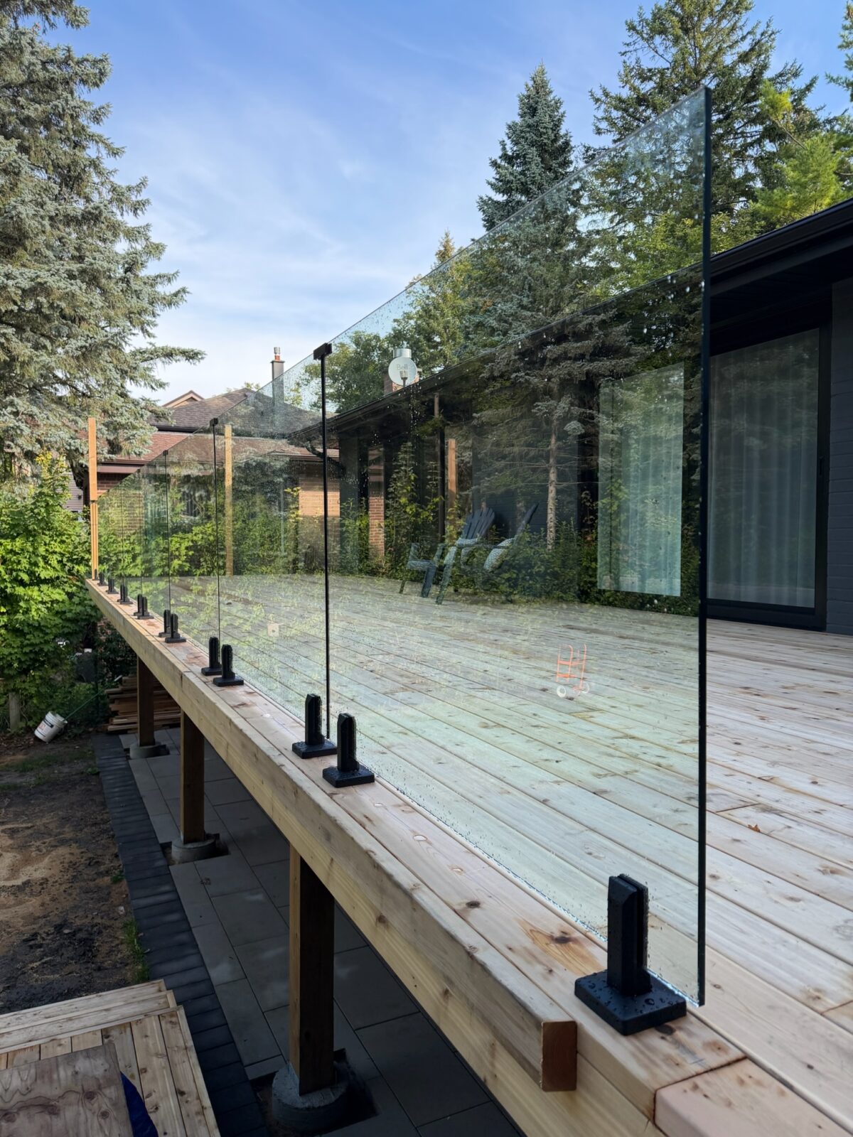 Frameless glass railing panels on black base shoes along a new cedar deck